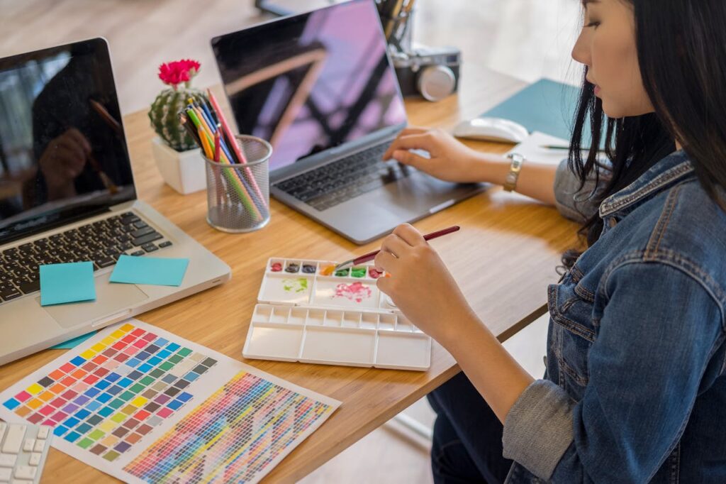 A woman using a laptop and painting with watercolors in a modern office environment.