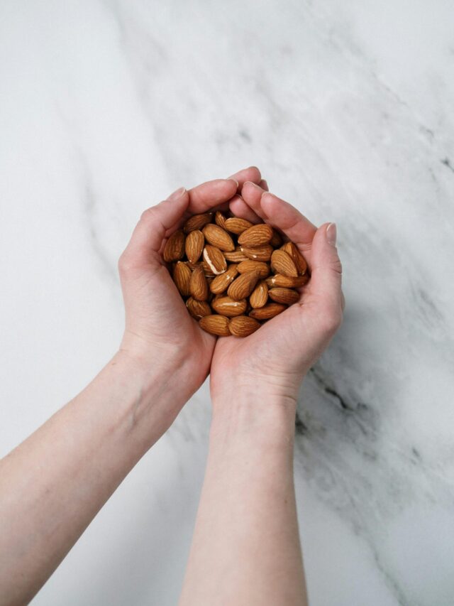 Two hands gently cupping a handful of almonds on a marble background, showcasing healthy snacks.