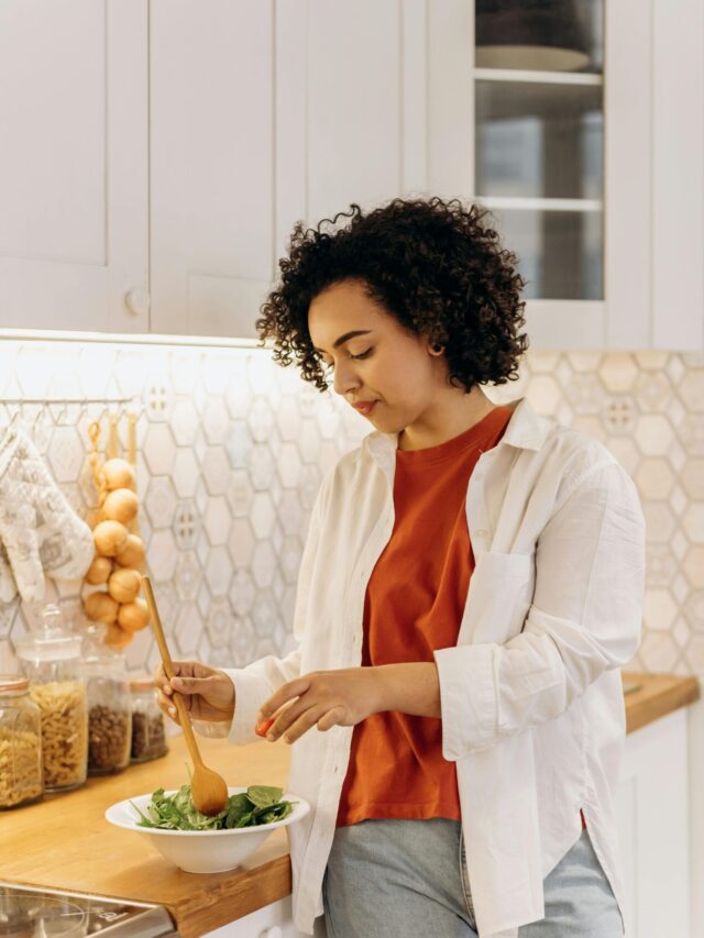 Curly-haired woman in a kitchen making a fresh salad, embracing a healthy lifestyle.