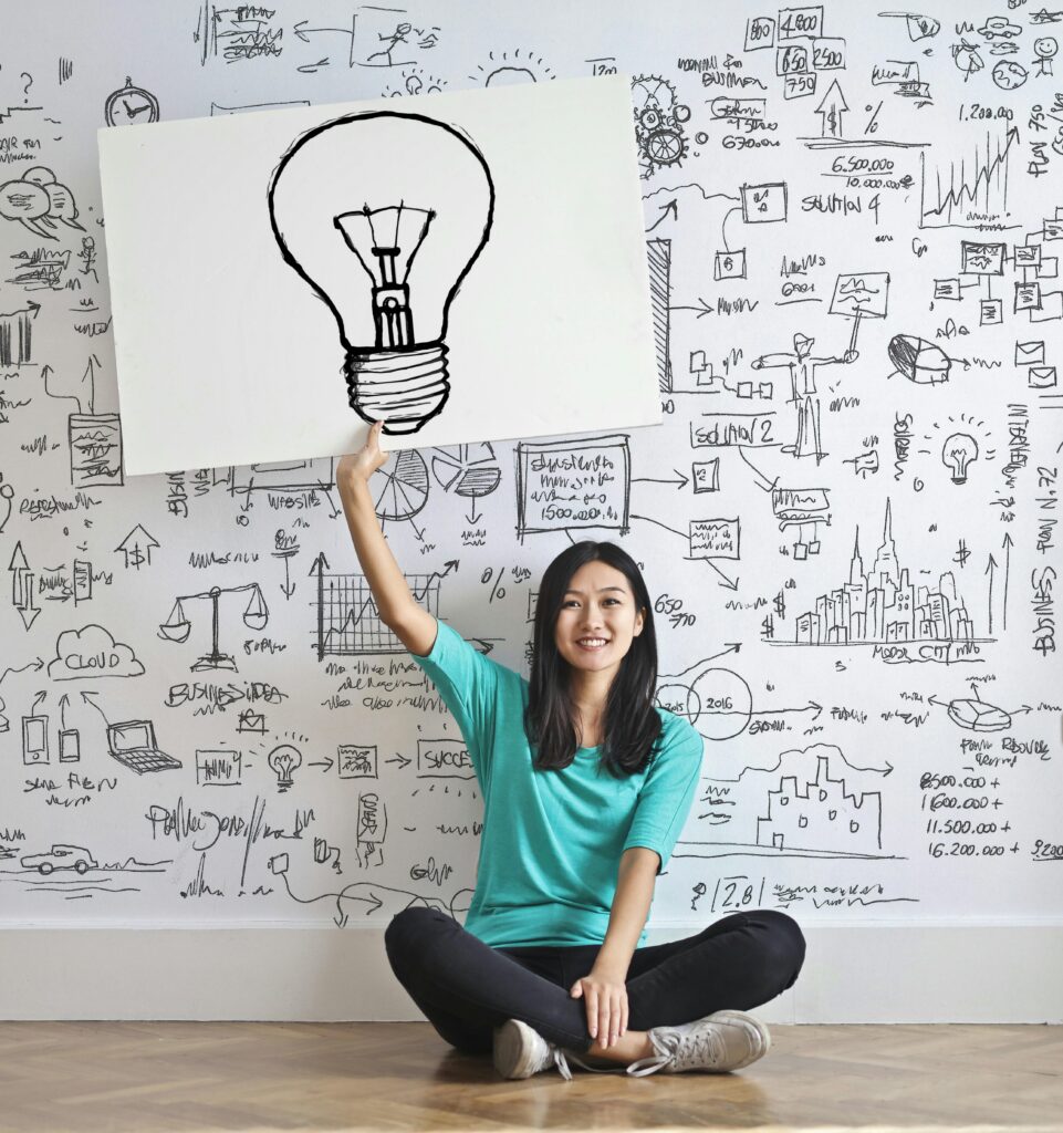 Young woman holds a light bulb drawing against a creative brainstorming wall.